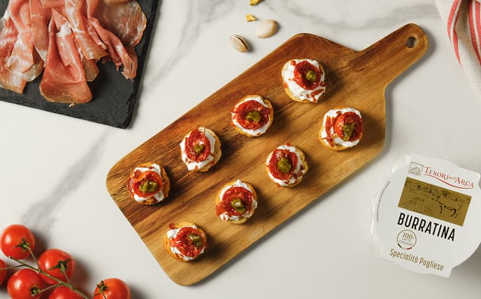 Mini bruschette con burrata, pomodorini confit, pesto e chips di prosciutto crudo